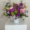 Mixed pink, purple, and green flowers arranged in a white vase