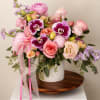 Pink and lavender floral arrangement in a white vase with ribbon