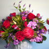 Bouquet of red roses, purple blooms, and a pink protea in a vase
