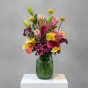 Colorful bouquet of lilies, calla lilies, and mums in a green glass vase
