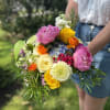 Handheld bouquet of pink, yellow, orange, and white flowers
