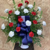 Red and white carnations in a white vase with a large blue ribbon