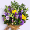 Hand-tied bouquet of purple and yellow flowers wrapped in brown paper