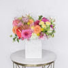 Bright mixed arrangement of pink, orange, and yellow flowers in a white square vase.