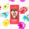 Red boxed chocolate bar with heart-shaped LOVE design surrounded by colorful daisies.