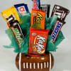 Candy bars arranged in a football-shaped ceramic container with green tissue paper