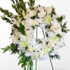 White floral wreath on a stand with lilies, roses, and daisies