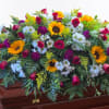 Large floral spray with sunflowers, roses, and white daisies on a wooden casket