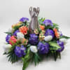 Purple and white floral arrangement with orange accents around a ceramic angel figurine
