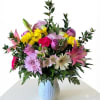 Mixed bouquet of pink, yellow, and lavender flowers in a white vase