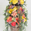 Tiered floral arrangement in a wooden basket with yellow, pink, and coral blooms