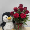 Red roses in a glass vase beside a plush penguin