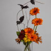 Orange gerbera daisies in a clear glass vase with autumn leaves