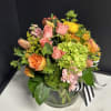 Mixed bouquet of pink, orange, yellow, and green flowers in a glass vase