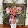 Pink roses and peonies arranged in a white vase with a ribbon