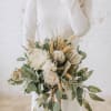 Bride holding a cream and green bouquet with roses and dried grasses