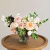 Mixed pastel flower arrangement in a glass vase on a wooden table