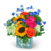 Mixed bouquet with sunflowers, roses, hydrangeas, and blue flowers in a glass vase