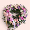 Heart-shaped floral wreath with pink, purple, and white flowers and a satin ribbon