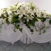 White floral arrangement with lilies and daisies on a draped table