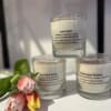 Set of three scented glass candles with printed labels, styled beside orange and yellow tulips.