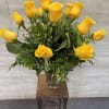 Tall arrangement of yellow roses in a clear glass vase on a wooden stand.