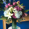 Bouquet of pink roses, lilies, hydrangeas, and blue delphinium in a glass vase