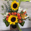 Tall floral arrangement with sunflowers, coral roses, and white blooms in a black vase