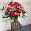 Bright pink roses, carnations, and mixed blooms in a clear glass vase on a small table