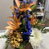 Orange lilies with blue delphinium and white chrysanthemums in a wood-look container