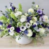 Mixed white, blue, and purple flowers in a white bowl vase