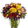 Mixed bouquet of yellow, red, purple, and pink flowers in a clear glass vase