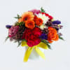 Mixed bouquet of roses, gerbera daisies, and chrysanthemums in a white vase with yellow ribbon