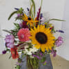 Mixed bouquet with sunflowers, pink blooms, and purple flowers in a glass vase