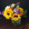 Mixed bouquet with sunflowers, daisies, and purple flowers in a glass vase