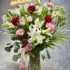 Mixed bouquet of red roses, white lilies, and pink carnations in a glass vase