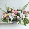 Low floral arrangement with pink blooms, white orchids, and green accents in a gray vase