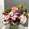 Mixed pink, purple, and orange flowers arranged in a green glass vase.