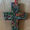 Colorful beaded mosaic cross ornament with a red hanging ribbon on a wood surface