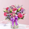 Pink roses and lilies in a glass vase with a purple ribbon