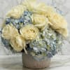 Low arrangement of ivory roses and pale blue hydrangeas in a round ceramic vase