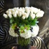White roses and green orchids in a tall glass vase