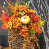 Autumn floral arrangement in a woven basket with orange flowers and a small pumpkin