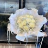 Bouquet of pale yellow roses wrapped in white paper with ribbon accents