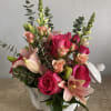 Pink roses and lilies arranged in a white ceramic teapot.