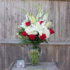 White lilies and red roses in a glass vase with a candle holder nearby
