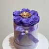Purple roses in a round lavender box with a gold rose center and ribbon bow