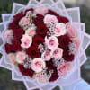 Round hand-tied bouquet of red and light pink roses with tiny white filler flowers in pink decorative wrap