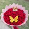 Handheld bouquet of red roses wrapped in pink paper with a gold butterfly and crown decoration.