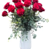 Red roses arranged in a white vase with trailing greenery